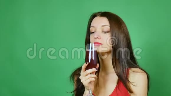 美丽的女孩微笑着举起一杯酒敬酒她穿着一件红色的球衣绿色背景视频的预览图