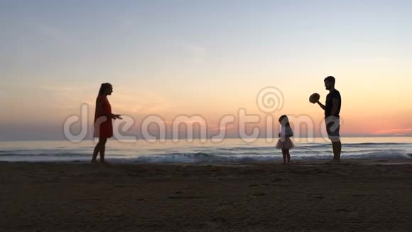 日落时小女孩沿着海滩在父母之间奔跑视频的预览图