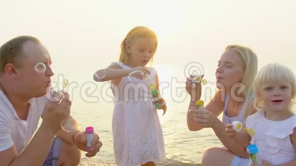 快乐的四口之家在美丽的日落中在海滩上玩肥皂泡快乐的度假时光慢慢地视频的预览图