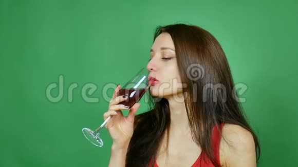 这位深色头发的妇女在绿色背景下喝着玻璃杯酒女孩穿着红色摔跤服视频的预览图