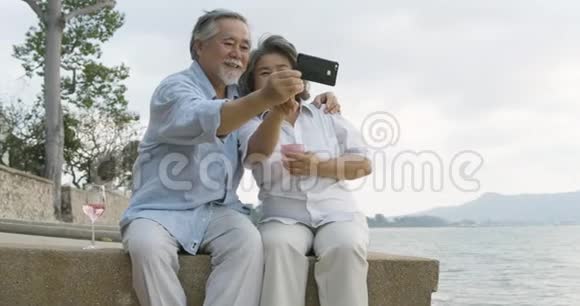浪漫的亚洲老年夫妇在美丽的热带海滩上看日落享受一杯葡萄酒视频的预览图