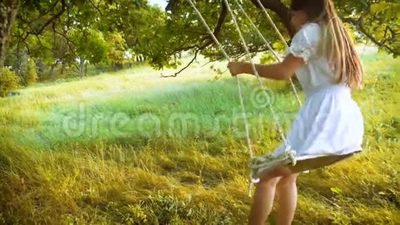 美丽的女孩长发在秋千上摆动在夏天的公园里笑慢动作视频的预览图