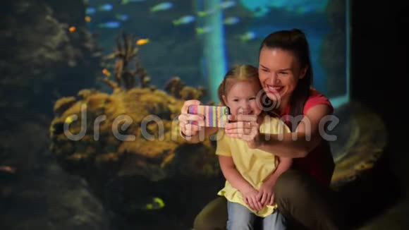 快乐的母亲和女儿正在自拍有鱼的水族馆就在后台他们有很多乐趣这位母亲视频的预览图
