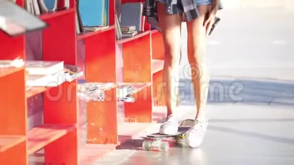滑板上的一个漂亮女孩走到街上的书架前选择了一本书视频的预览图