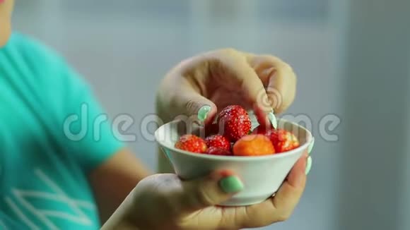 一个女人正在从白色盘子里摘一个草莓然后吃它相机在看手视频的预览图