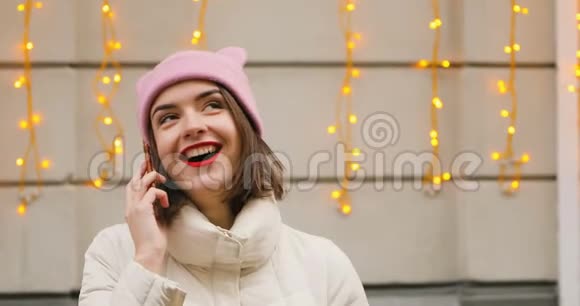布鲁内特漂亮的年轻女性肖像戴着可爱的粉红色帽子红唇微笑调情在电话里交谈圣诞节视频的预览图