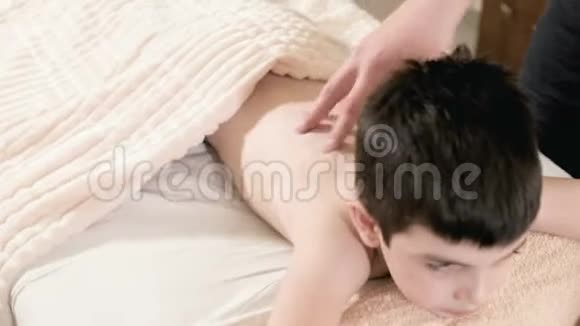 特写男理疗师按摩师为躺在按摩床上的小男孩做一个疗愈放松的按摩回去视频的预览图