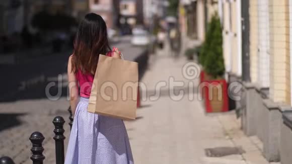 一位年轻漂亮的女士带着纸袋在慢动作购物后转身微笑视频的预览图