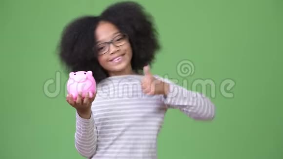 年轻可爱的非洲女孩非洲头发手里拿着储蓄罐竖起大拇指视频的预览图