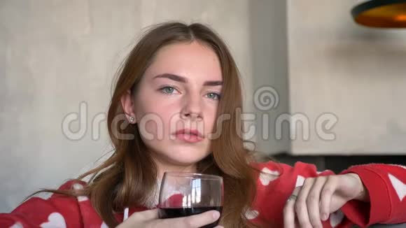 一位留着姜发看着相机端着酒杯坐在现代沙发上的美女画像视频的预览图