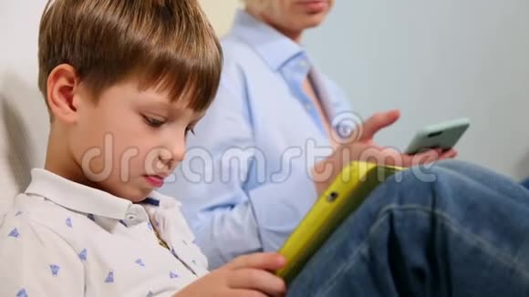 一家三口坐在沙发上使用数字设备那个男孩用平板电脑和母亲浏览关于视频的预览图