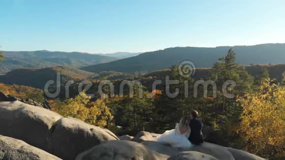 日落时分爱的情侣坐在山上的岩石上视频的预览图