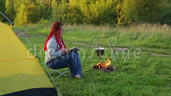 一个女人靠近篝火帐篷看着沸腾的锅视频的预览图