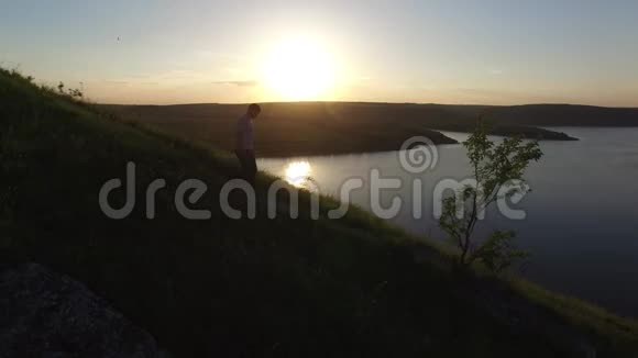 空中史诗拍摄一个人在河岸边散步作为一个轮廓在美丽的日落视频的预览图