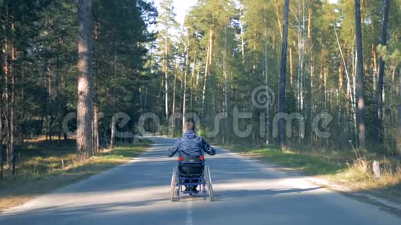 一位残疾人坐在轮椅上沿着森林道路行进的后景视频的预览图