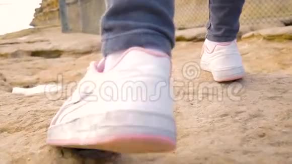 一个穿着白色运动鞋和灰色牛仔裤的年轻女孩的脚特写她走过浮雕的岩石棕色表面视频的预览图