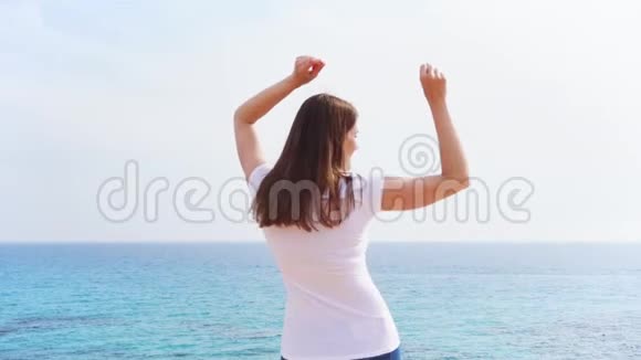 阳光明媚的一天女人在悬崖上与蔚蓝的大海欢快地跳跃无护理女性慢动作舞蹈视频的预览图
