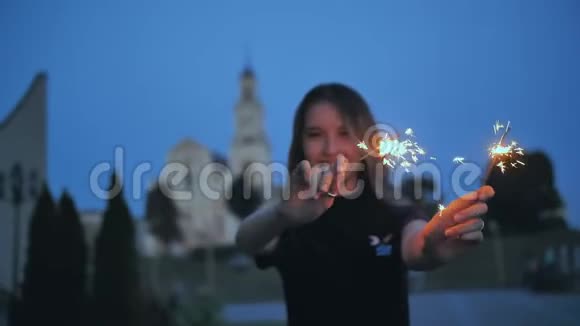 女孩在晚城的背景下用闪闪发光的手挥动着视频的预览图