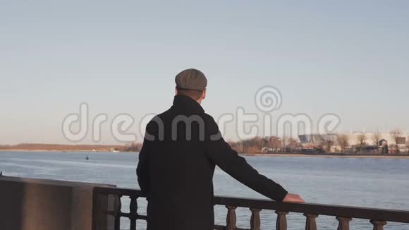 一个穿着优雅的年轻人站在河边若有所思地看着远处抓着栏杆视频的预览图