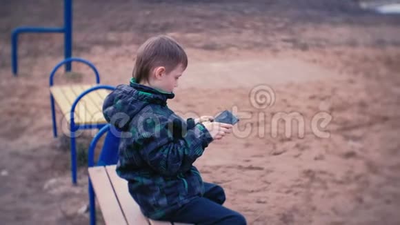 男孩坐在公园的长凳上玩游戏侧视图视频的预览图