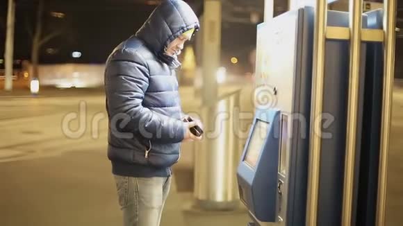 一个穿暖和夹克的成年人用停车机的触摸屏来支付停车费用视频的预览图