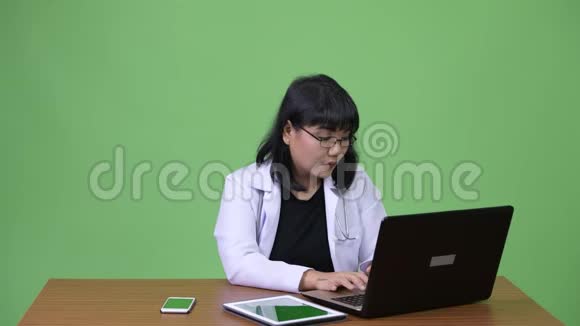 美丽的亚洲女医生多任务和工作中的视频呼叫视频的预览图