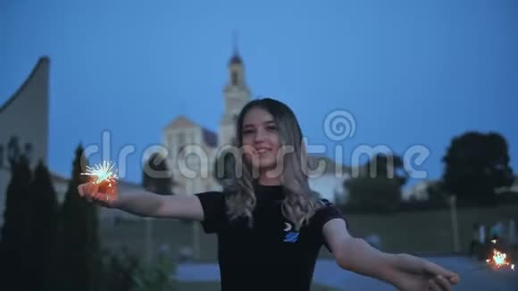 女孩在晚城的背景下用闪闪发光的手挥动着视频的预览图