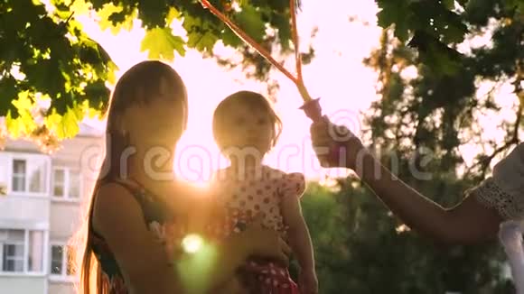 妈妈和她的小女儿在城市公园里捉到了又大又透明的肥皂泡笑了视频的预览图