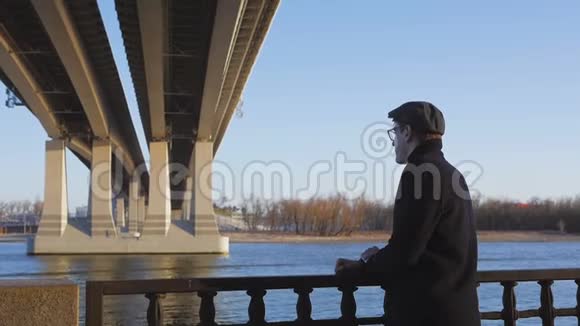 一个穿着优雅的年轻人站在河边若有所思地看着远处抓着栏杆视频的预览图