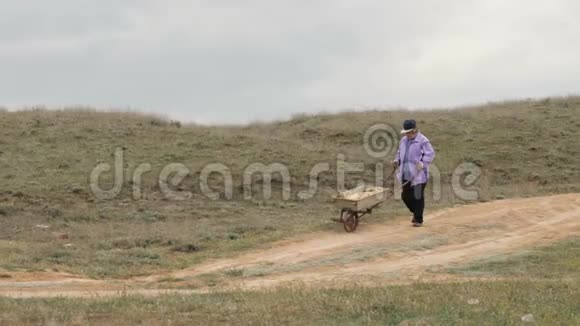 老园丁妇女走在乡间小路上推着花车视频的预览图