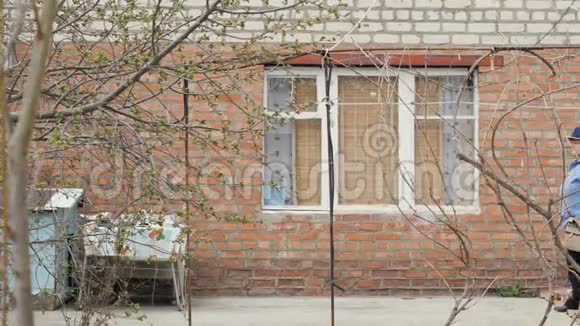 带着水壶的老妇人园丁走在背景休息大楼里视频的预览图