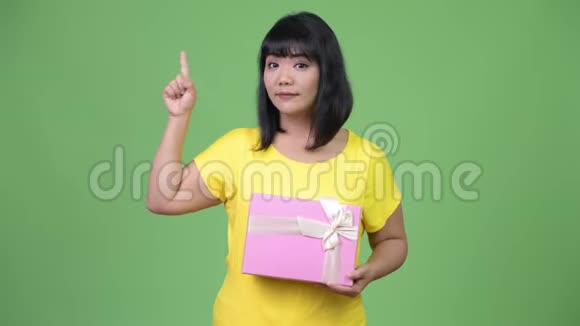美丽快乐的亚洲女人一边拿着礼品盒一边指着视频的预览图