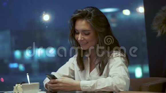 女孩独自坐在咖啡馆里使用智能手机灯光背景下一个少年在咖啡馆的画像视频的预览图