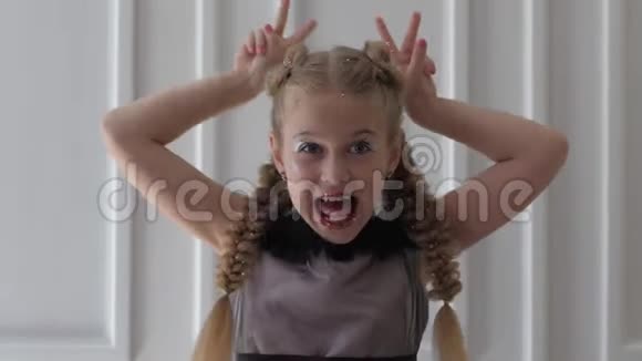 带着辫子和闪亮的化妆笑着的孩子在室内做滑稽的面孔视频的预览图