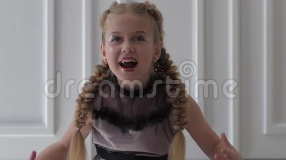 带着辫子和闪亮的化妆笑着的小女孩在室内做滑稽的表情视频的预览图