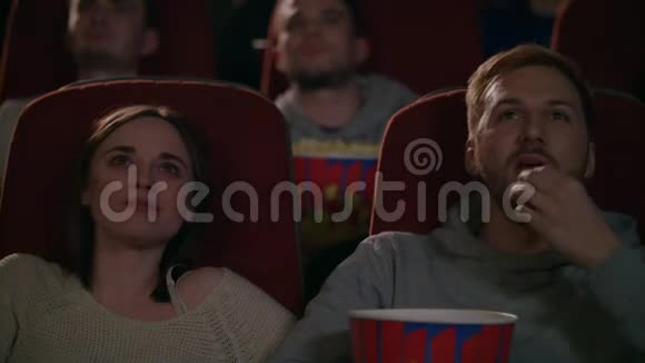 年轻夫妇在电影院欣赏电影两个人吃爆米花讨论电影视频的预览图