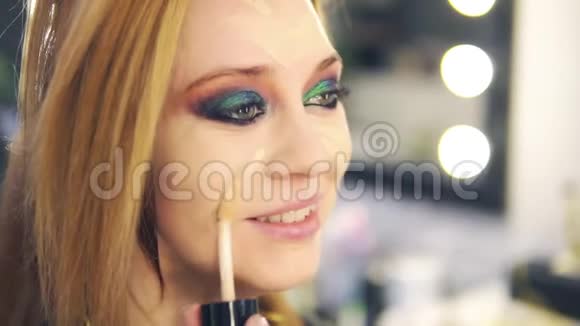 来访者用棍子在年轻微笑的女人脸上涂上液体基础沙龙专业化妆侧视图视频的预览图