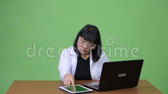 美丽的亚洲女医生戴着防护眼镜工作时多任务视频的预览图