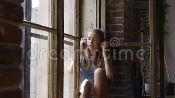 橱窗背景上年轻漂亮女孩的画像是戴着耳机听音乐一个漂亮的少女坐着视频的预览图