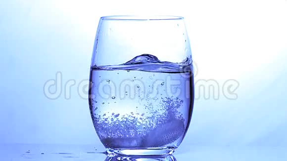在蓝色背景下落入一杯水中的药片视频的预览图