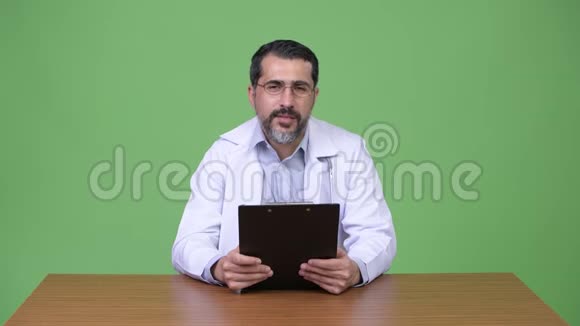 英俊的波斯胡子男医生一边拿着剪贴板一边会诊视频的预览图