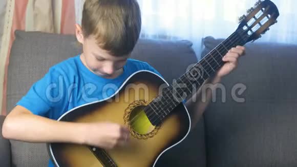 男孩学会坐在沙发上弹吉他学习演奏乐器的概念视频的预览图
