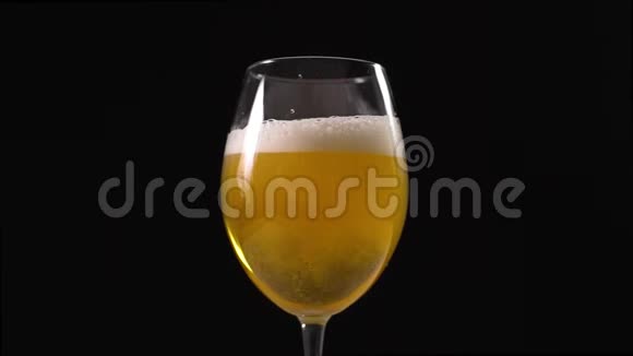 金色泡沫啤酒缓慢地倒入玻璃杯中黑色背景下的啤酒杯啤酒中的气泡淡啤酒视频的预览图