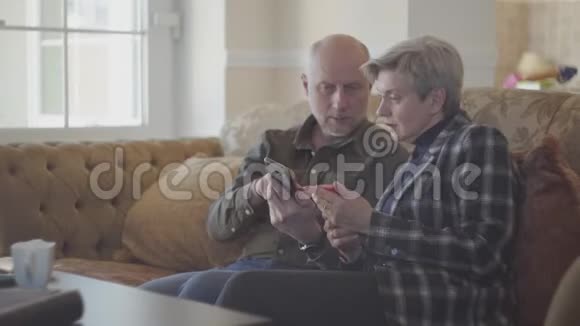 老两口坐在大沙发上秃头在手机上为他的短发女人展示照片视频的预览图