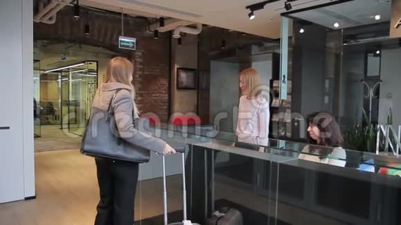 在接待处带手提箱的女士受到酒店工作人员的愉快欢迎视频的预览图