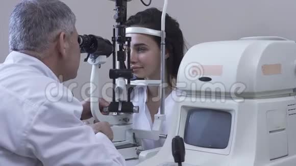 一位年轻漂亮的女士坐在诊所里做眼科检查她正坐在医生面前穿着白色的医用外套看着验眼机视频的预览图