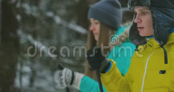 冬天一个穿黄色夹克的男人和一个穿蓝色连衣裙的女人在树林里慢动作滑雪视频的预览图