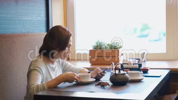 女人在咖啡馆喝茶手里拿着智能手机一位女士查看她的智能手机上的电子邮件并在视频的预览图