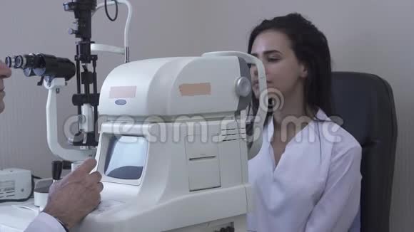 漂亮的年轻女子在诊所做眼科检查坐在医生面前穿着白色的医疗外套看着现代的眼科检查视频的预览图