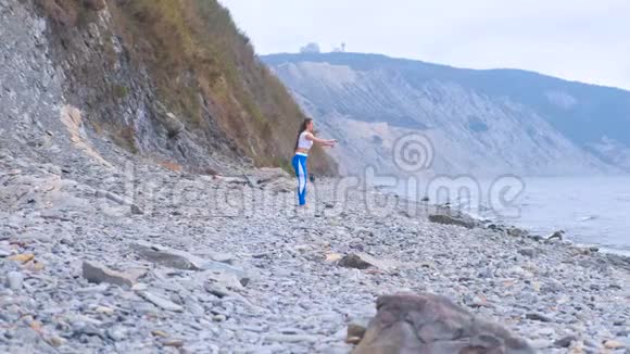 年轻女子在石滩上靠山做蹲式练习视频的预览图
